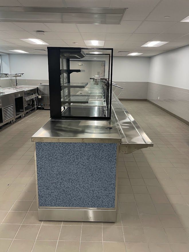 A commercial food service counter with a blue-speckled front panel, stainless steel surface, and a glass sneeze guard.