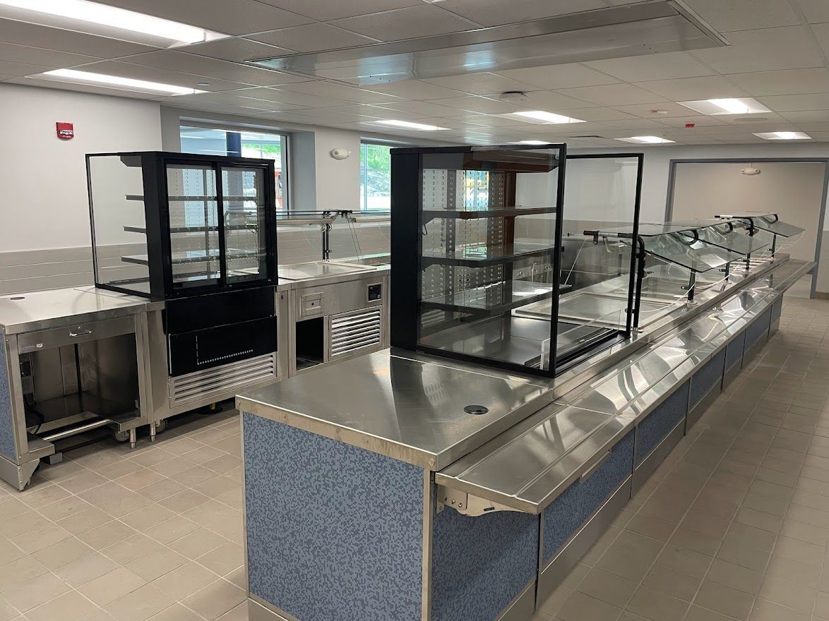 A cafeteria serving line with stainless steel counters and glass display cases set in a bright, modern room.