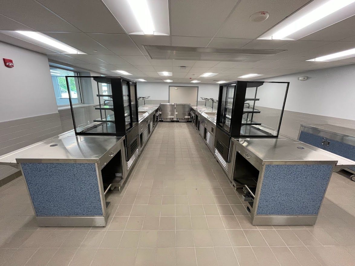A symmetrical view of a food service line with stainless steel counters and black display cases in a neutral room.