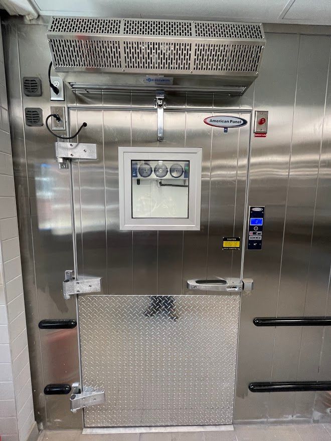 Stainless steel walk-in cooler door with an overhead cooling unit, window, diamond-plate kickplate, and digital display.