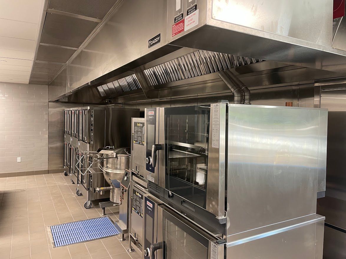 A professional industrial kitchen featuring large stainless steel convection ovens under an overhead ventilation hood.