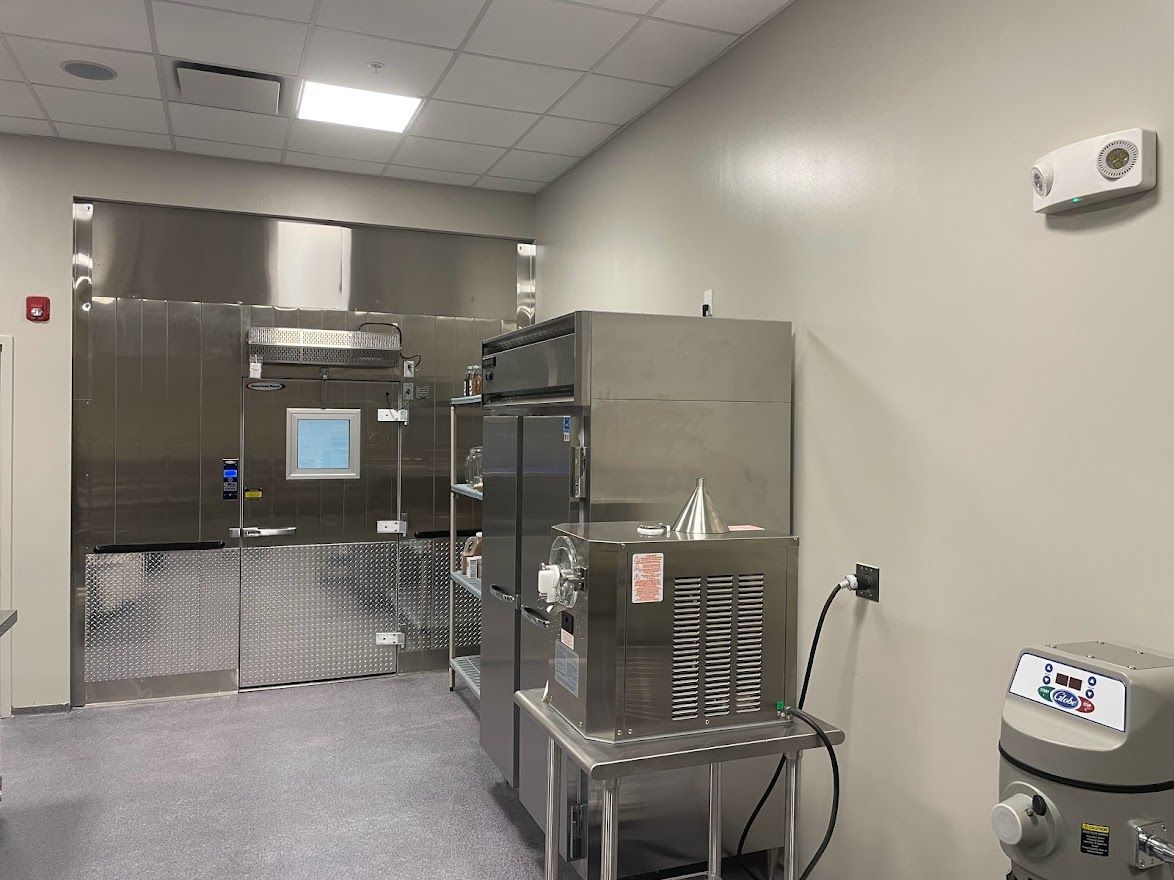 A stainless-steel lab or commercial kitchen area featuring a walk-in unit, refrigeration equipment, and tiled flooring.