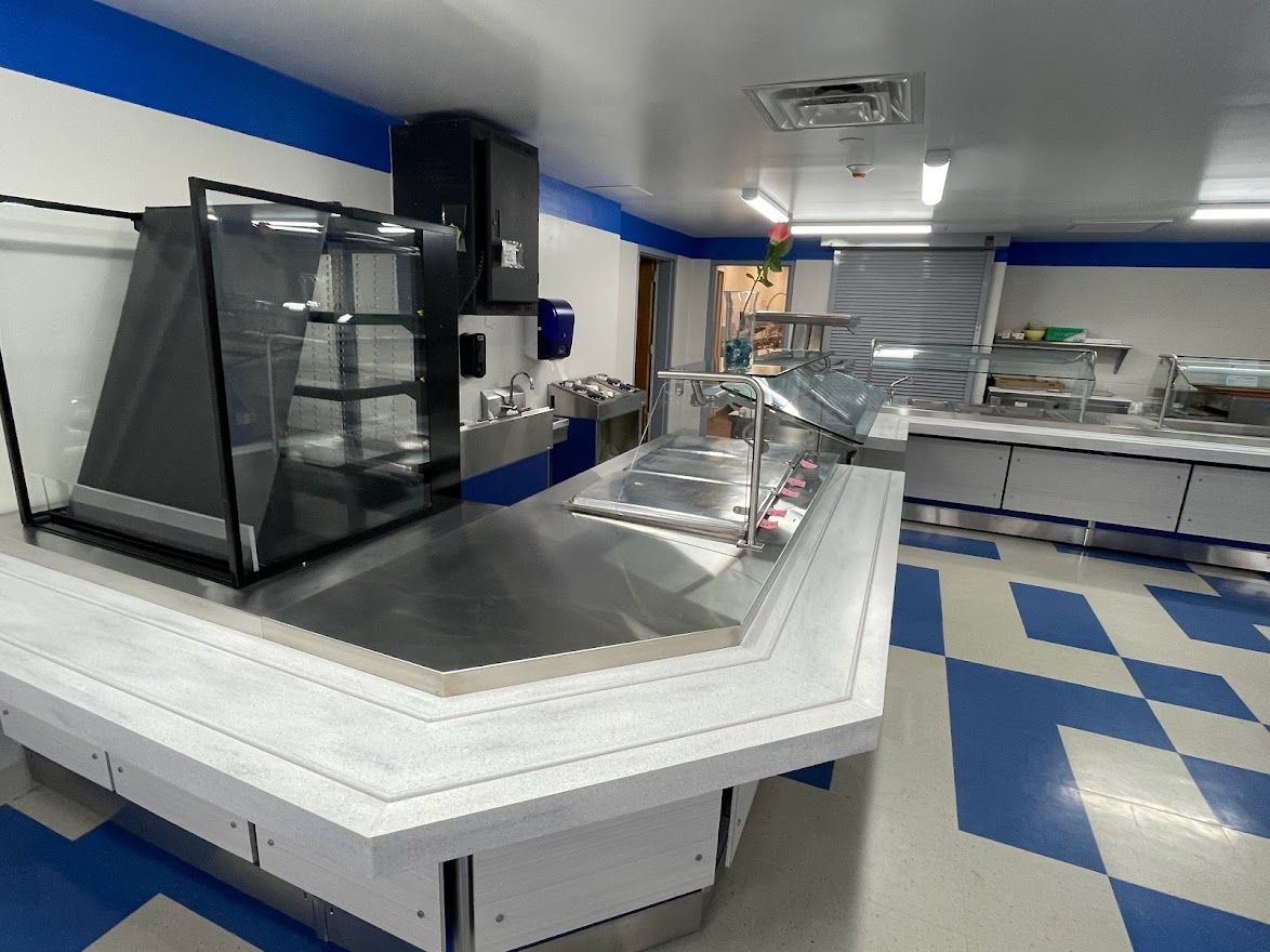 A commercial cafeteria serving line with a stainless steel counter and glass display case on a blue and white tiled floor.