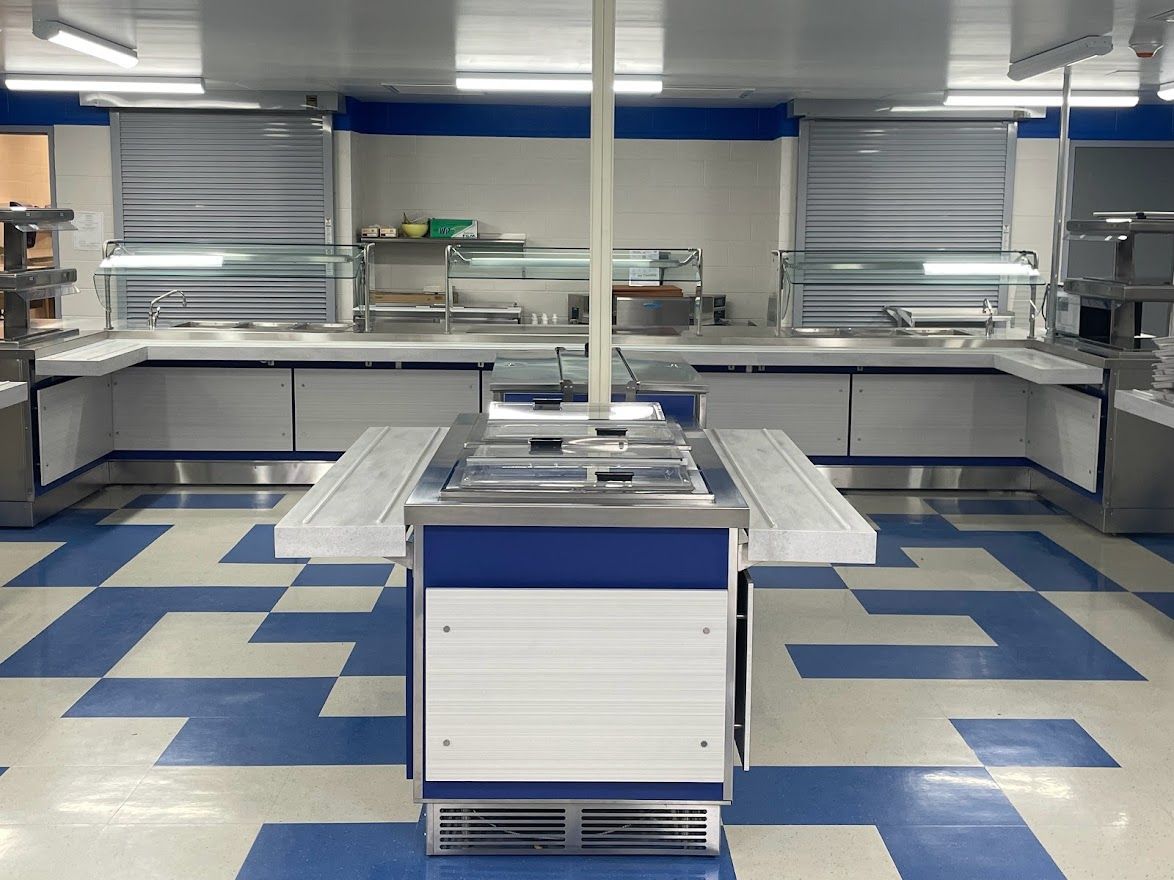 A stainless steel cafeteria serving line with a center island, blue and white decor, and blue and beige tiled flooring.