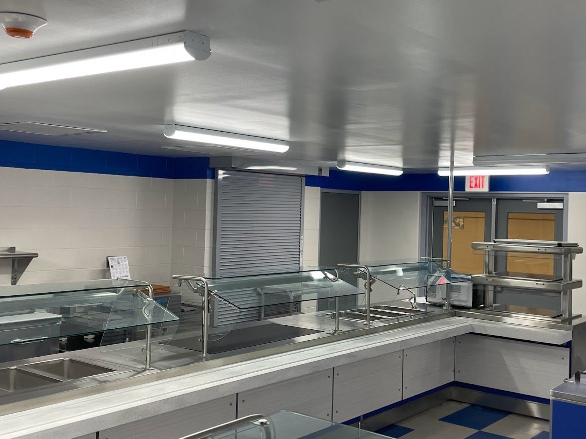 A serving line in a commercial cafeteria with stainless steel counters, glass sneeze guards, and bright overhead lights.