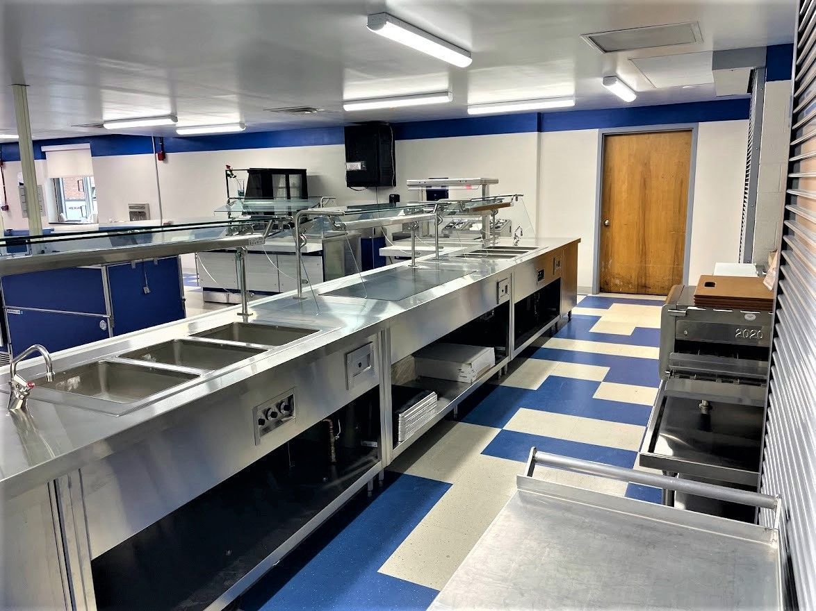 A commercial kitchen featuring stainless steel prep tables, sinks, and a blue and white tiled floor.