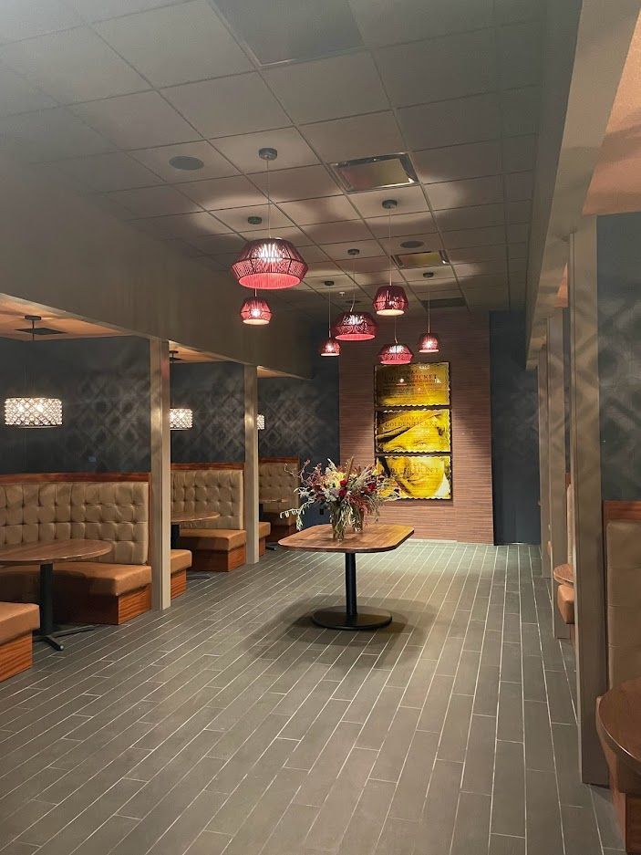 A dim restaurant interior featuring brown booth seating, dark wooden tables, tiled floors, and decorative red lamps.