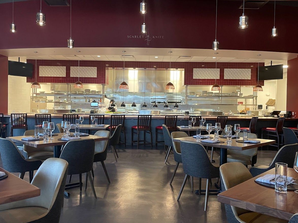 A view of a restaurant interior featuring a bar with stools, tables with chairs, and overhead pendant lighting.