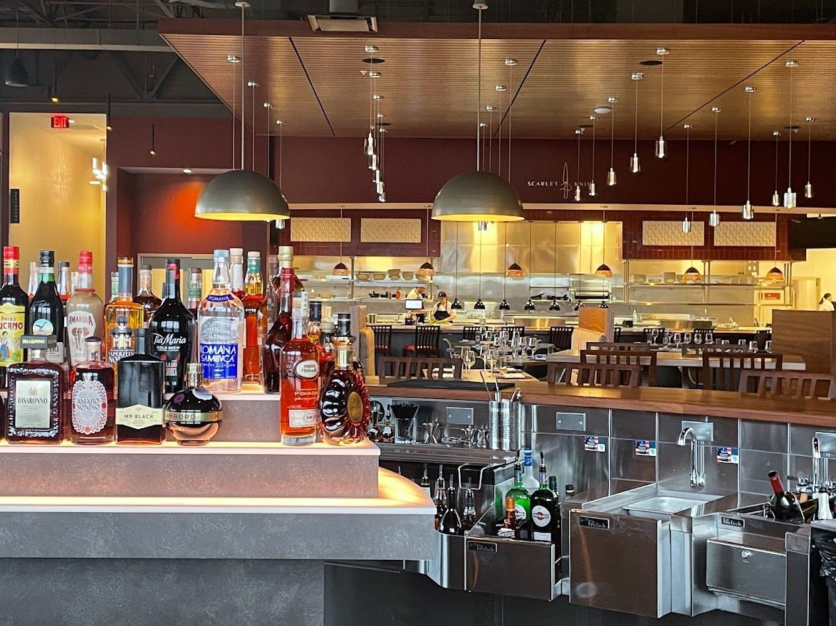 An illuminated bar featuring a tiered display of assorted liquor bottles under modern pendant lighting in a dining room.