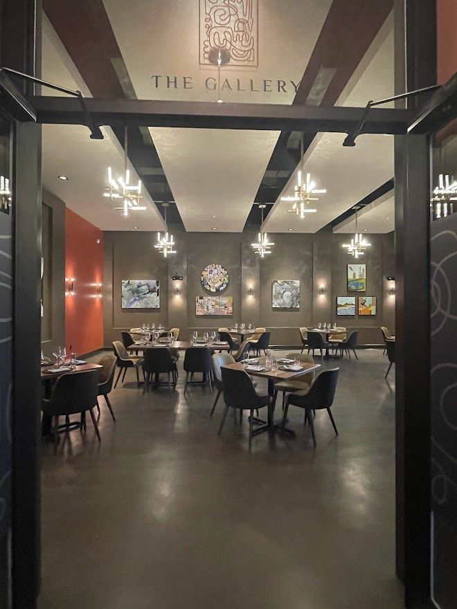 An interior view of a restaurant named The Gallery, featuring tables, chairs, modern lighting, and art on the walls.