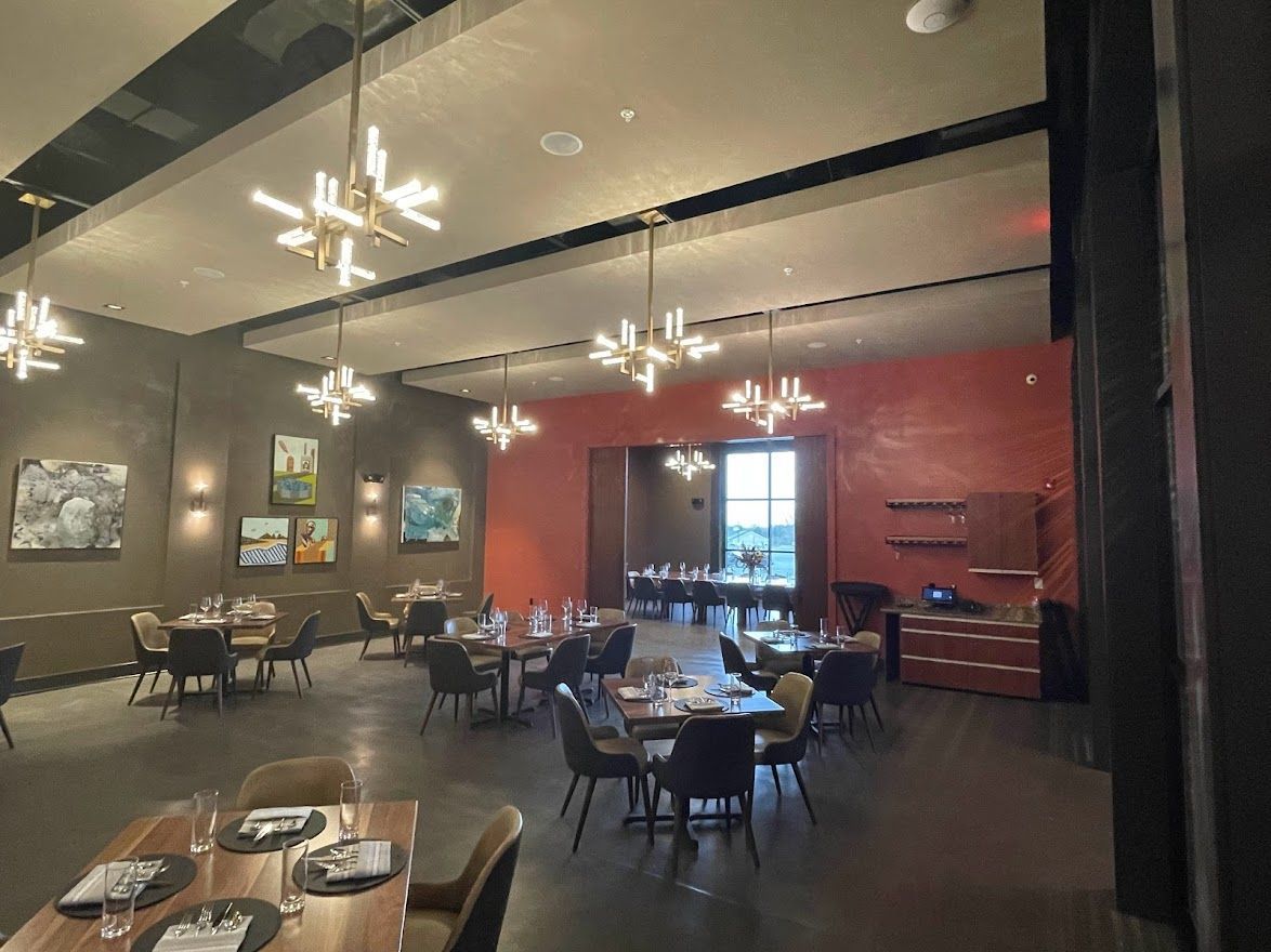 An upscale restaurant interior with tables, dark chairs, unique modern light fixtures, and a prominent red accent wall.