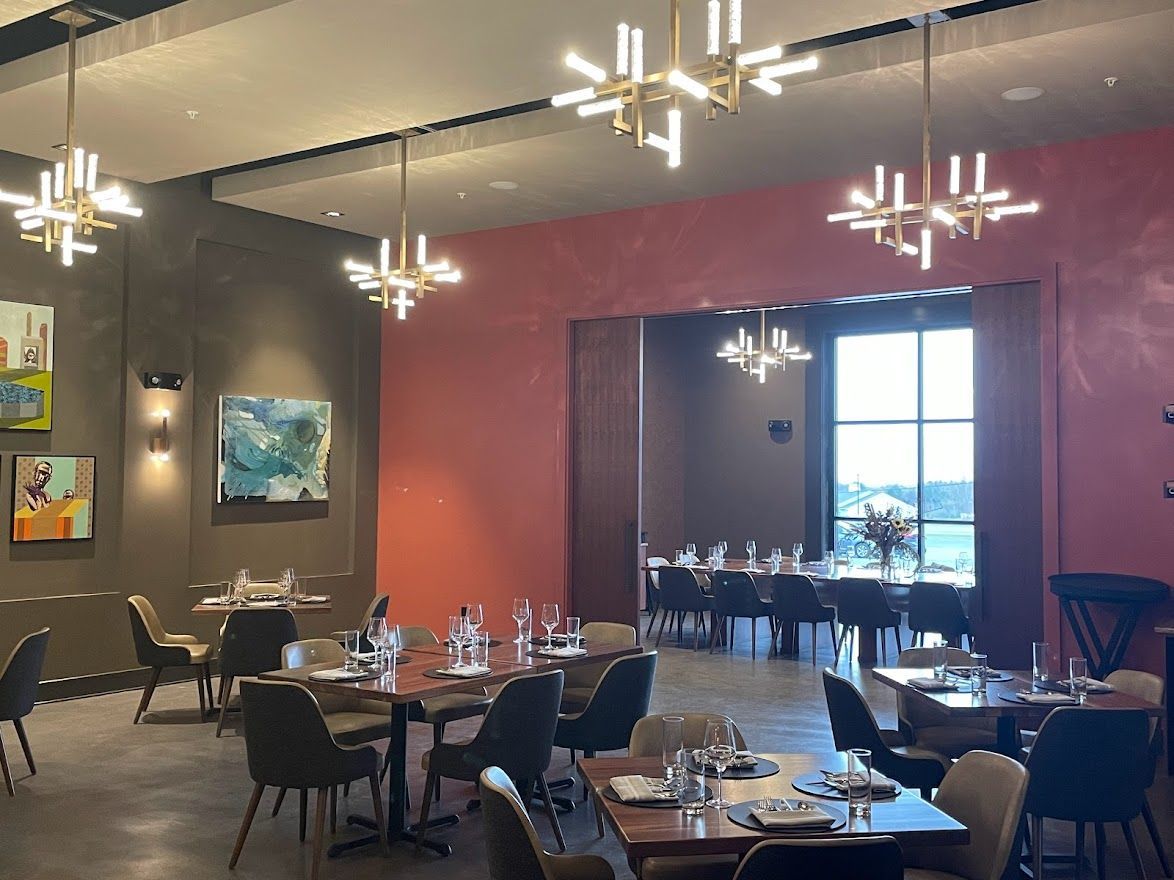 A dining room with wooden tables, dark chairs, modern light fixtures, and abstract art on pink and grey walls.