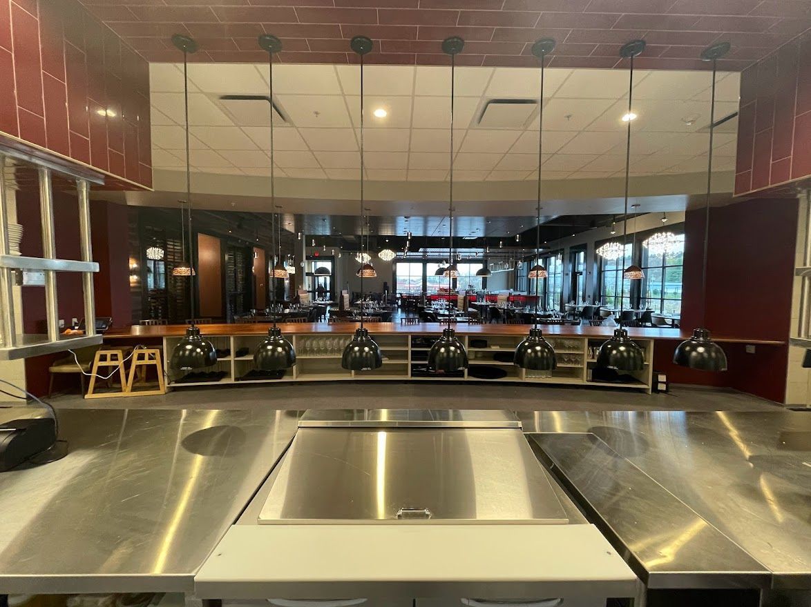 A wide-angle view of a restaurant kitchen counter with stainless steel surfaces and a row of hanging pendant lights.