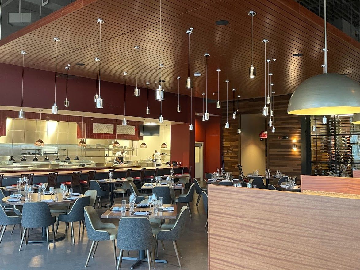 An elegant, modern restaurant interior with tables, grey chairs, warm pendant lighting, and a textured wood ceiling.