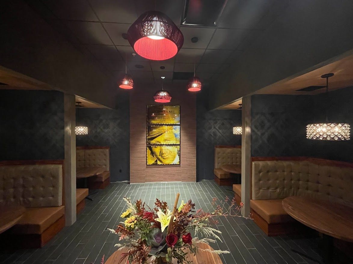 A symmetrical view of a dimly lit restaurant featuring brown tufted booths, hanging light fixtures, and a central artwork.