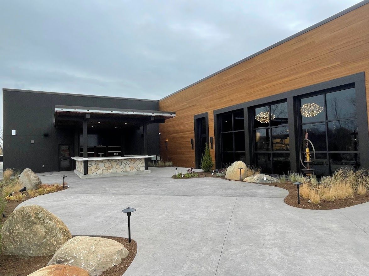 An outdoor patio with a stone-topped bar, concrete flooring, and large windows on a building with brown and black siding.