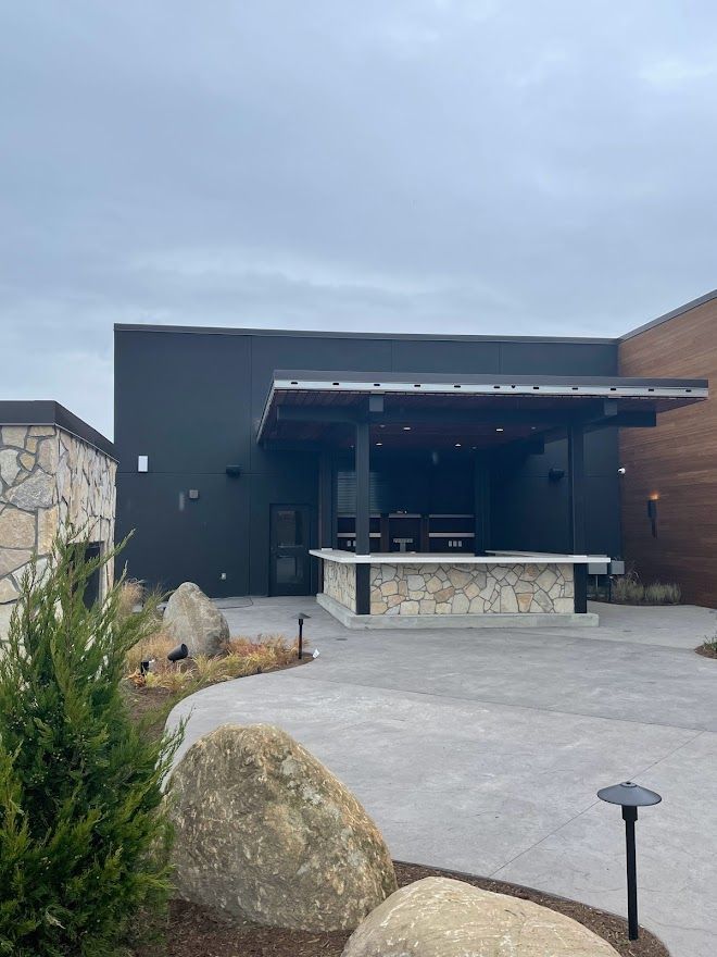 A modern outdoor patio bar with a stone counter, a dark covered roof, and large decorative boulders in the foreground.