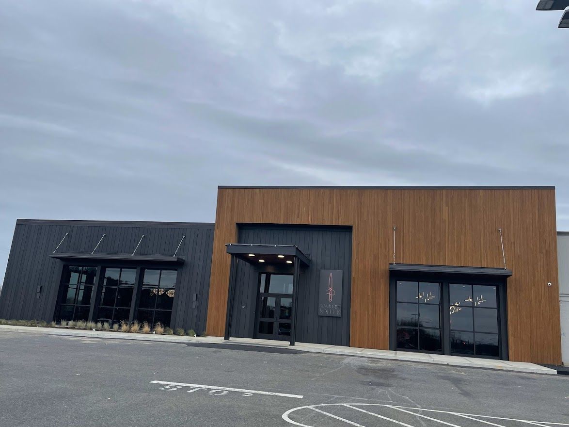 A modern commercial building exterior with a mix of dark gray vertical slats and natural wood-toned panels under a sky.