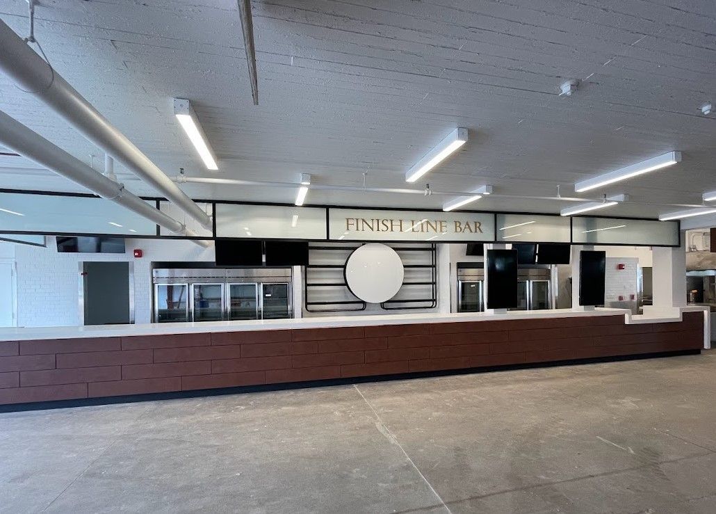 A long, empty bar with a brick facade and a central circular sign under a drop ceiling with industrial lighting.