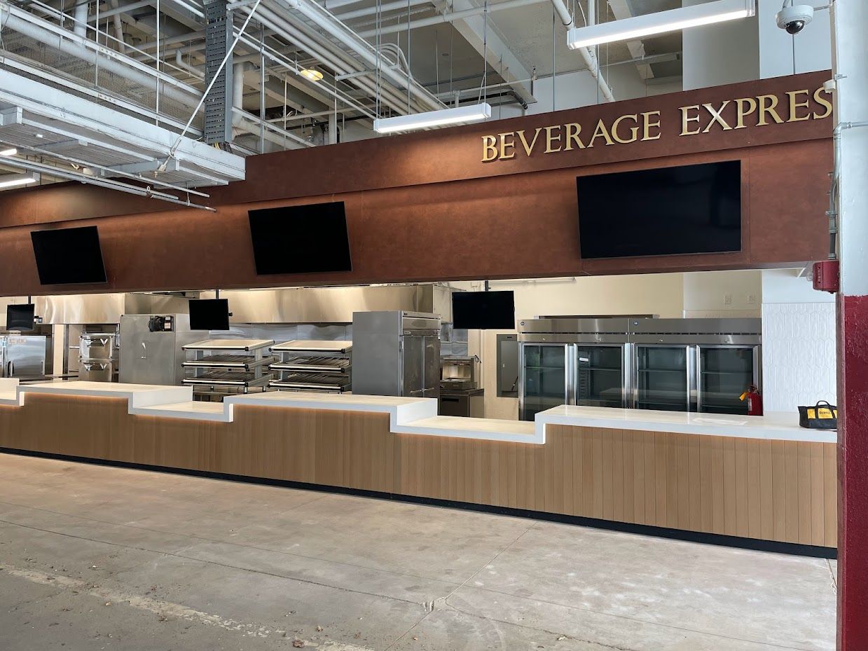 A beverage stand counter in an industrial-style setting with wood paneling, dark brown signage, and black display screens.