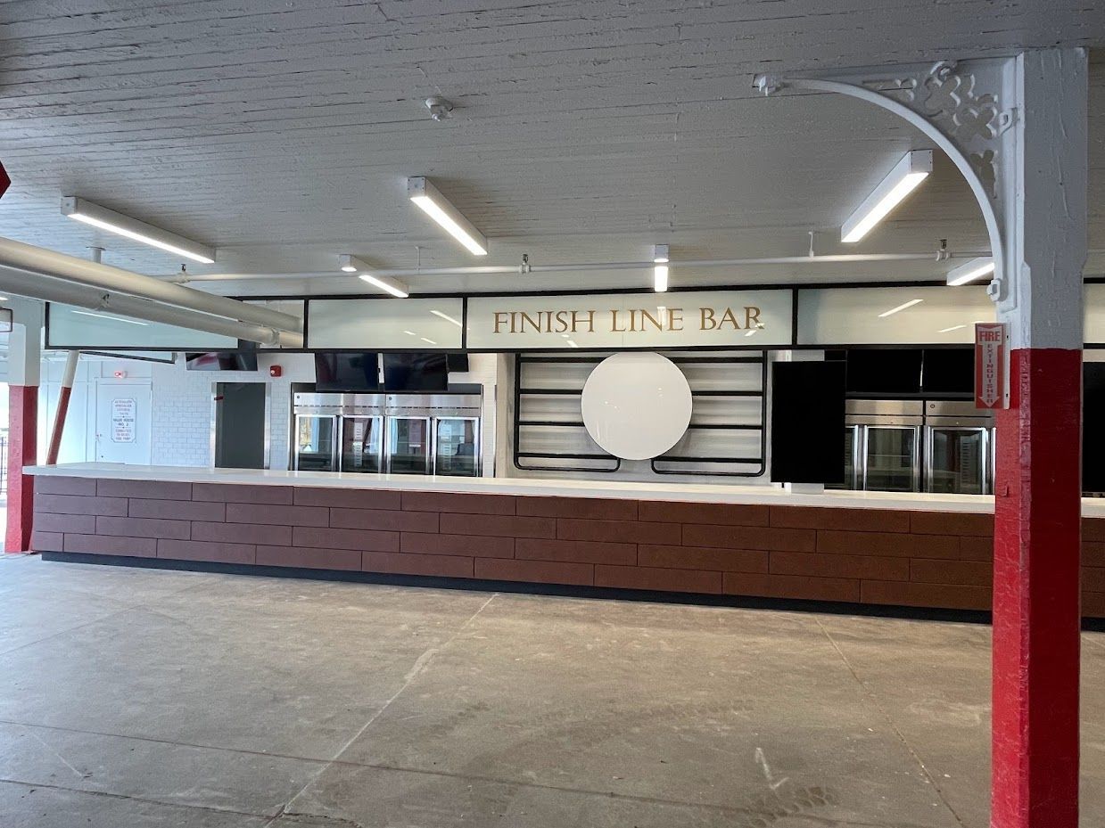 The Finish Line Bar features a long, brown wooden counter beneath fluorescent lighting in an open-air pavilion.