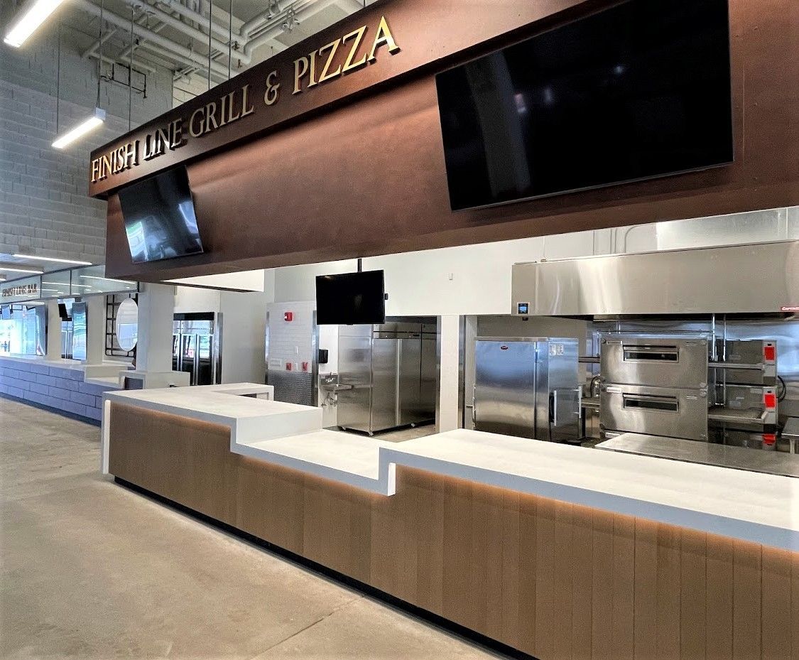 A view of a modern High Line Grill & Pizza counter with a white stone service top, wood-paneled base, and kitchen area.