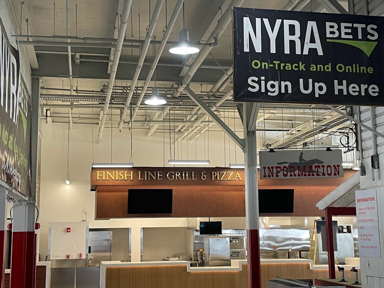 The interior of a venue featuring a Finish Line Grill & Pizza counter beneath a large NYRA Bets sign.