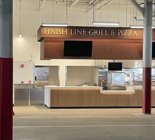 A Finish Line Grill & Pizza counter featuring a brown wooden sign, stainless steel surfaces, and pendant lights.