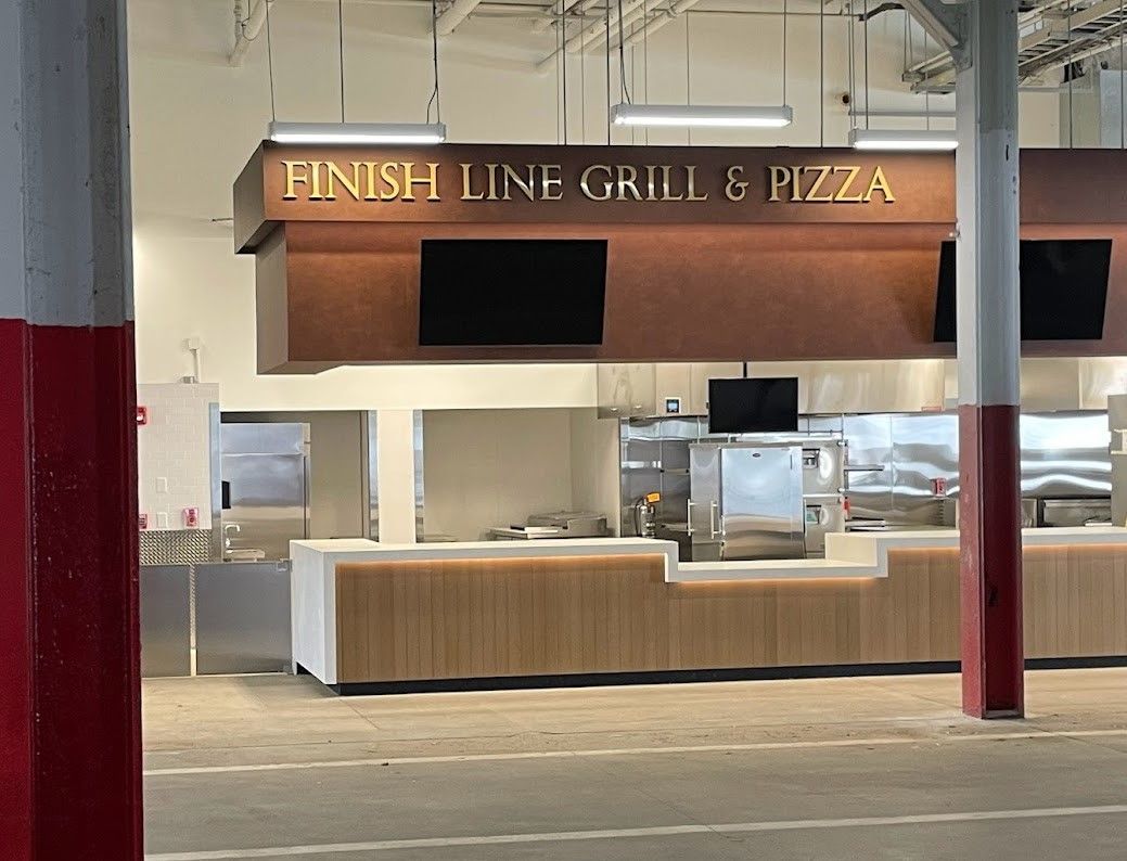 Finish Line Grill & Pizza food stall with a brown wood counter, black televisions, and red structural pillars.
