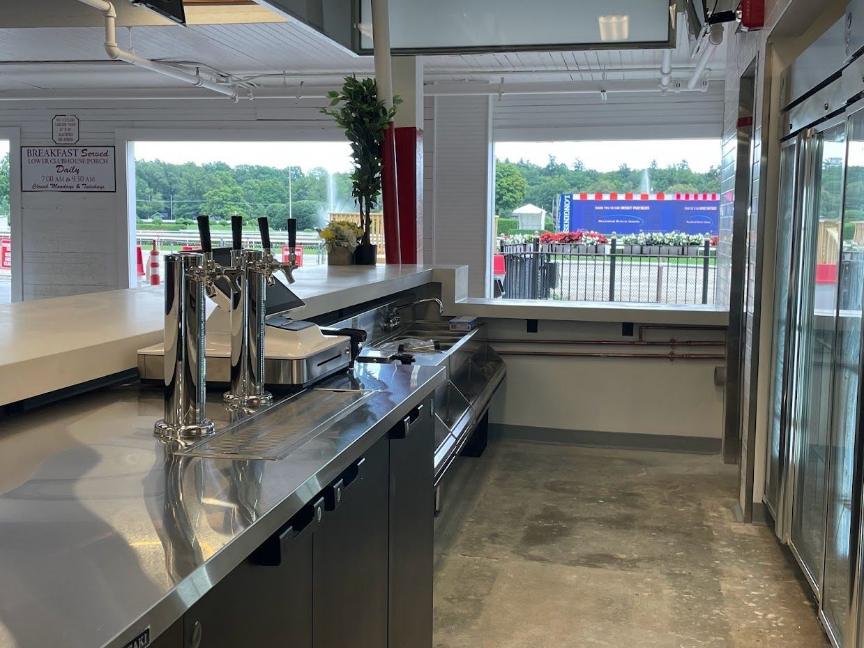 A stainless steel bar counter with beer taps, seen from behind the service area with an outdoor view in the background.