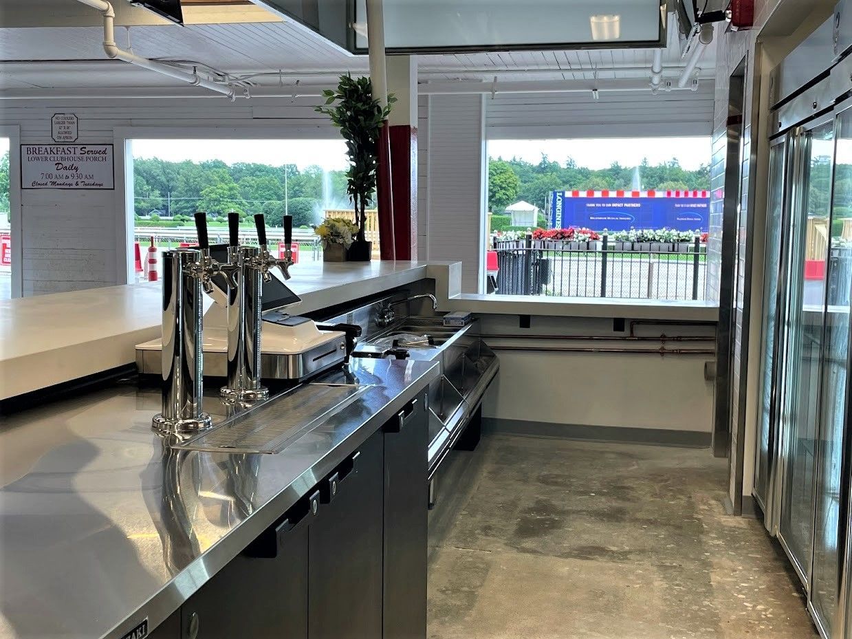 A stainless steel bar counter featuring two beer taps, situated in a brightly lit indoor space overlooking an outdoor area.