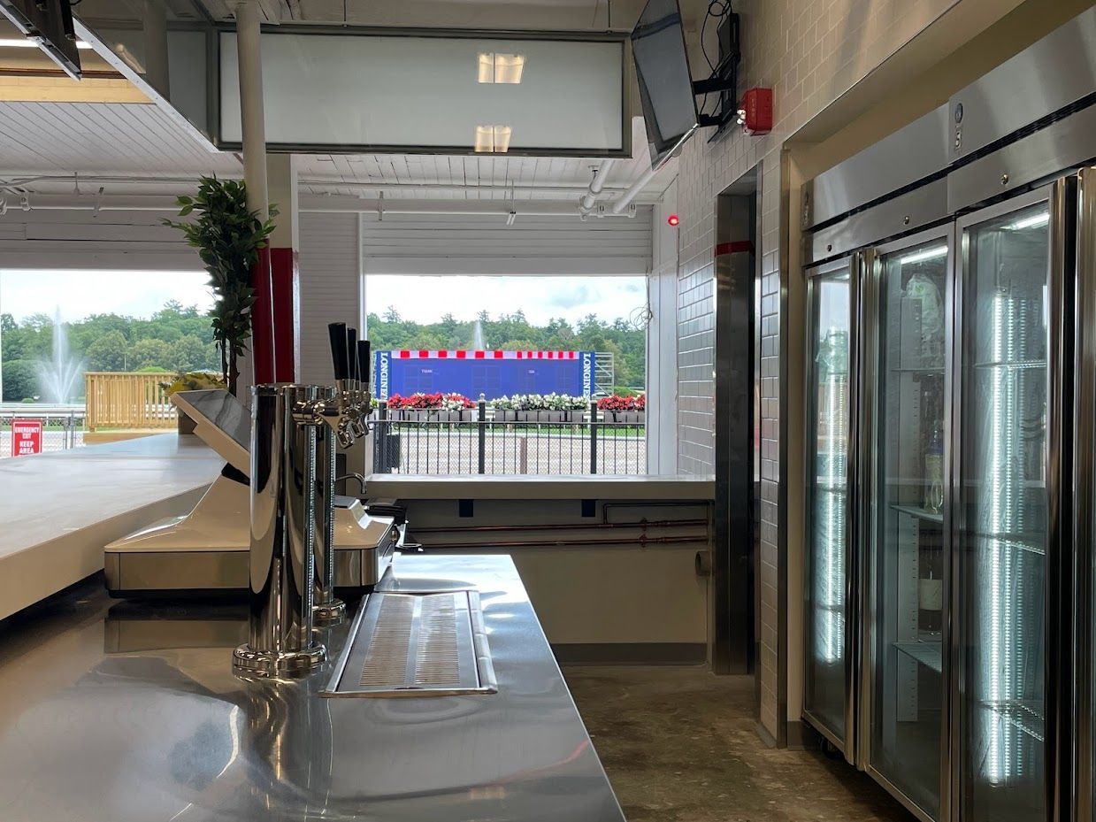 A bar area featuring beer taps, a stainless steel counter, and a glass-door cooler, with a view of an outdoor fountain.