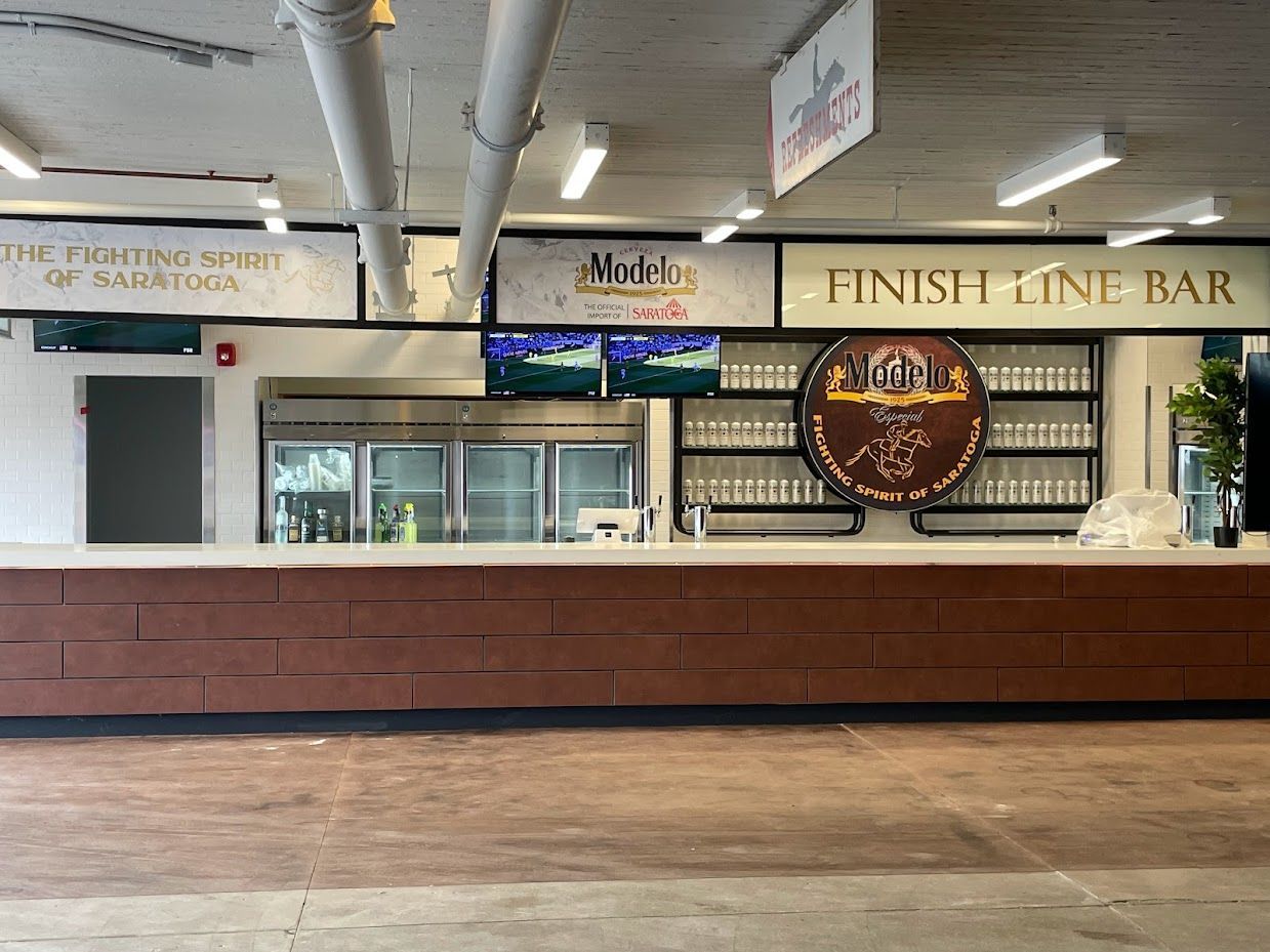 The Finish Line Bar features a long, dark wood counter, illuminated signage, and a circular logo under industrial ceilings.