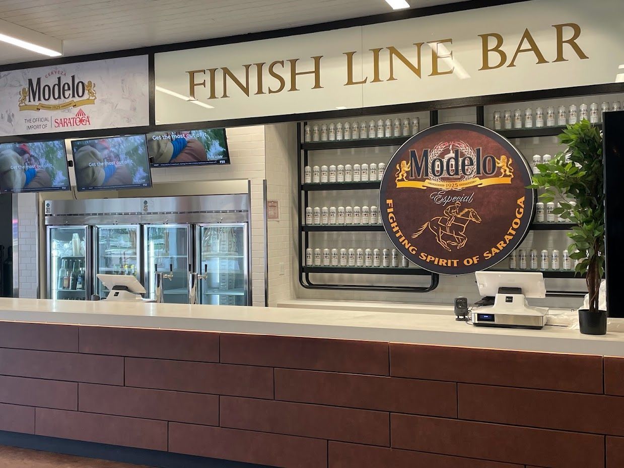 The Finish Line Bar features Modelo branding, a large circular sign, a long counter, and a wall of glass bottles.