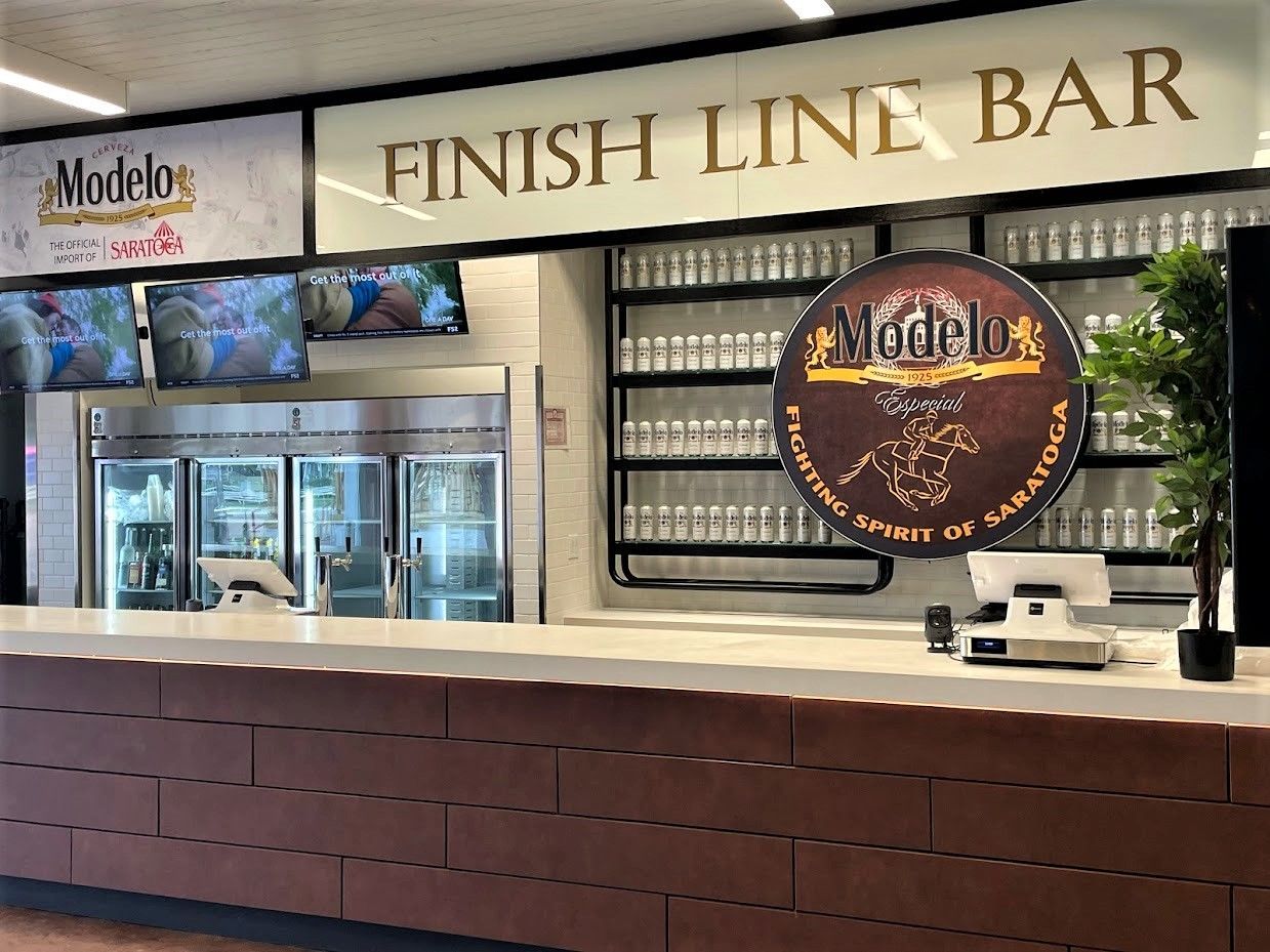 The Finish Line Bar features a Modelo-branded sign, a brick-patterned counter, glass beverage fridges, and a potted plant.