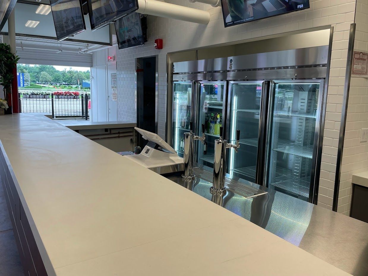A modern, clean bar area featuring a metal countertop, two beer taps, and a large three-door refrigerated display case.