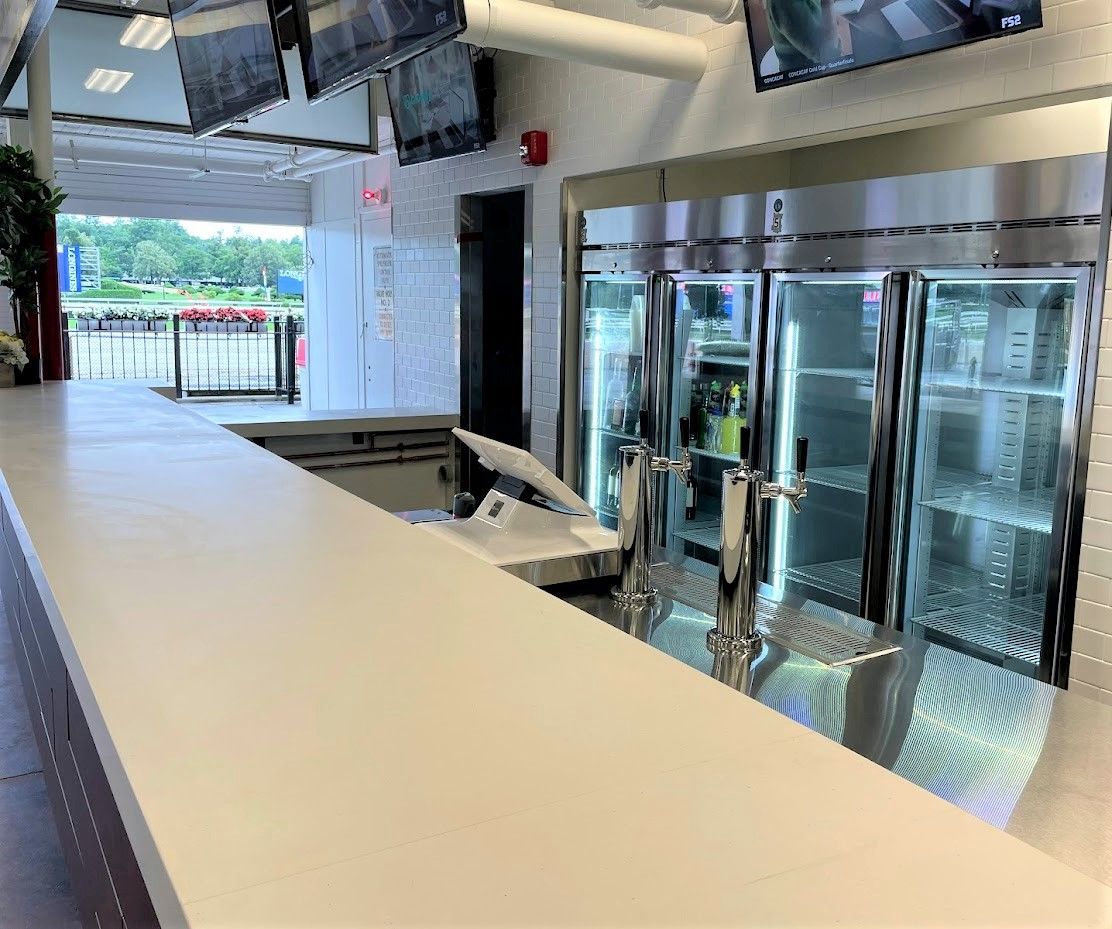 A view of a modern indoor bar counter with beer taps and refrigerated glass display cases, leading to an outdoor area.
