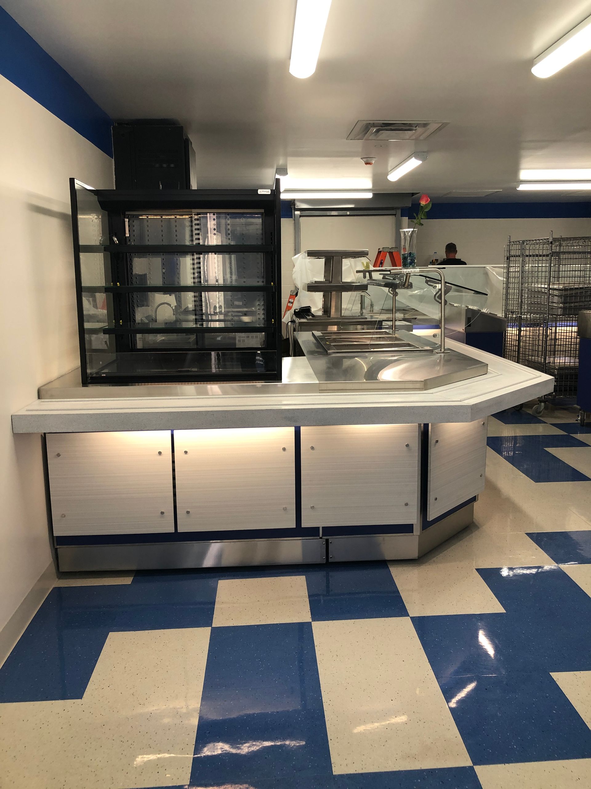 A food service counter with a display case, stainless steel surface, and under-counter lighting on a blue-and-white floor.