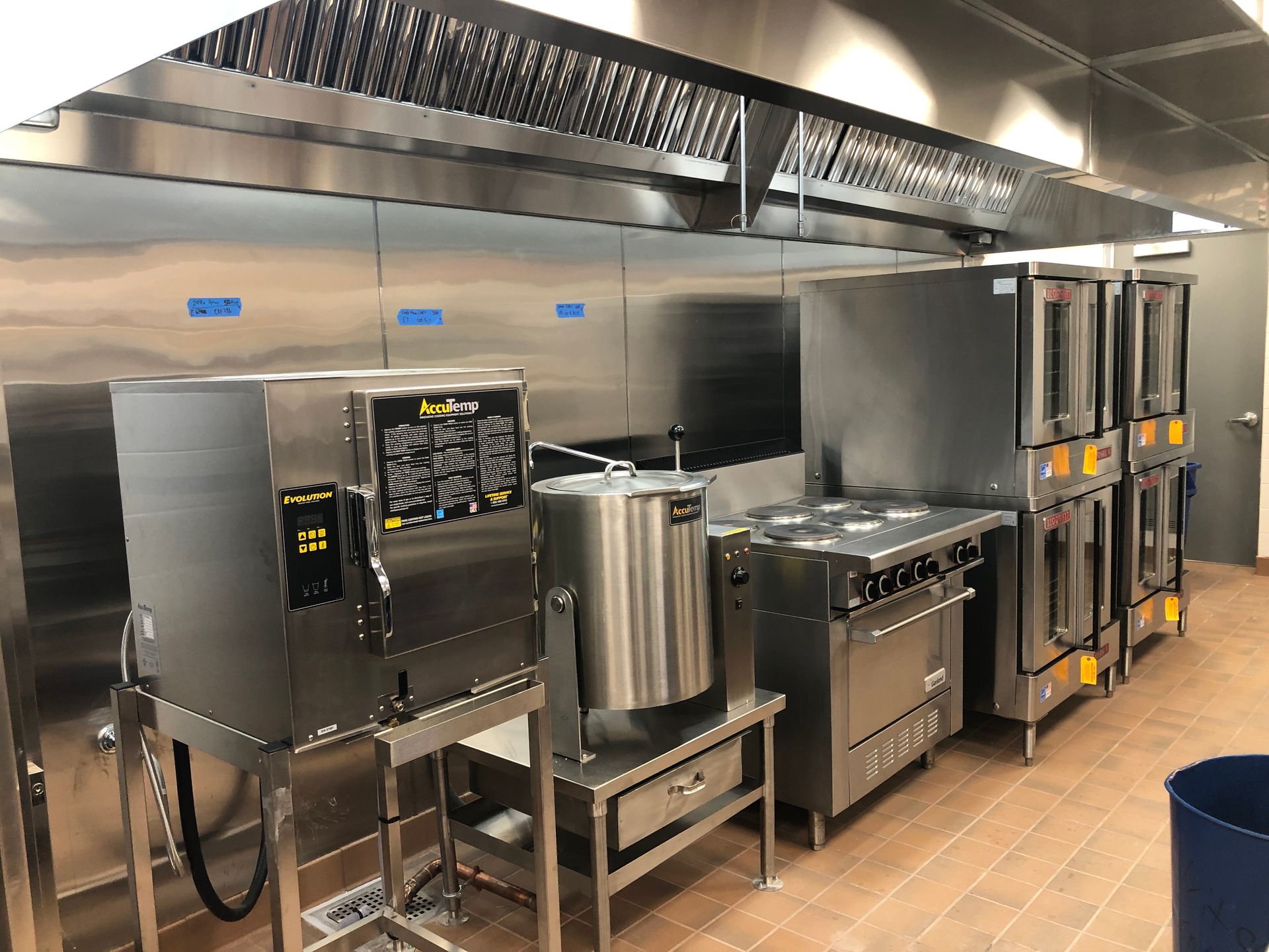 A professional commercial kitchen featuring stainless steel equipment, including a steamer, kettle, range, and ovens.