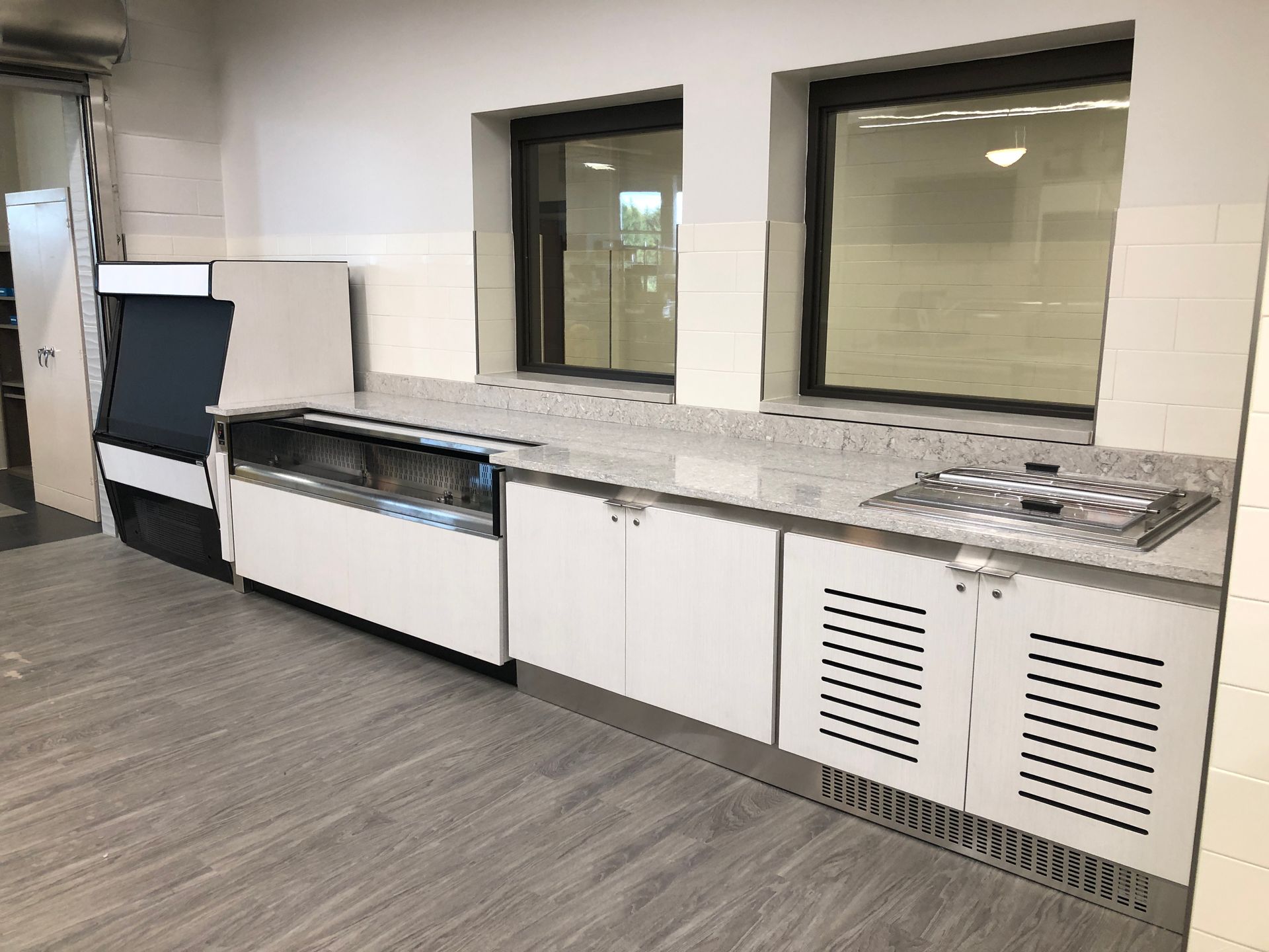 A modern commercial food service counter with white cabinets, a refrigerated display, and a stainless steel prep station.