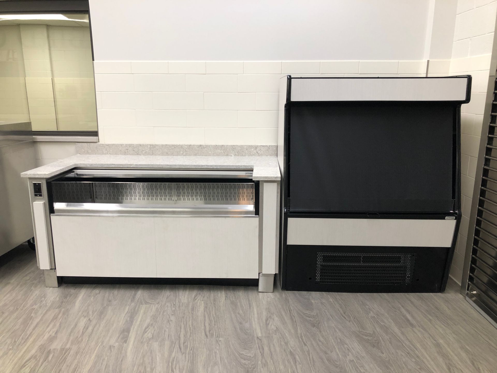 A low, white refrigerated deli case stands next to a tall, black and white vertical refrigerated display unit.