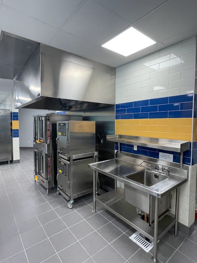 A commercial kitchen featuring stainless steel kitchen equipment, a double oven, and a metal sink under a ventilation hood.