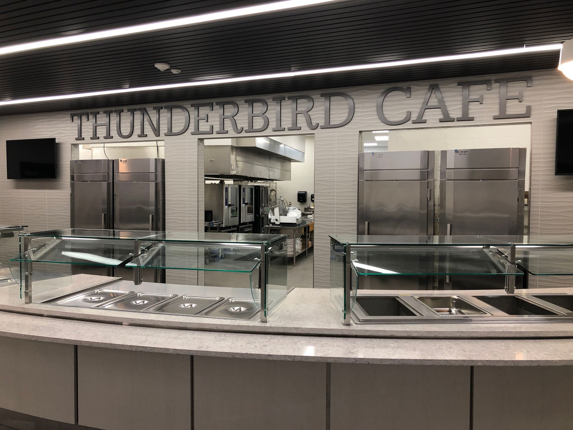 A modern serving line at Thunderbird Cafe, featuring stainless steel counters and appliances in a clean, brightly lit area.