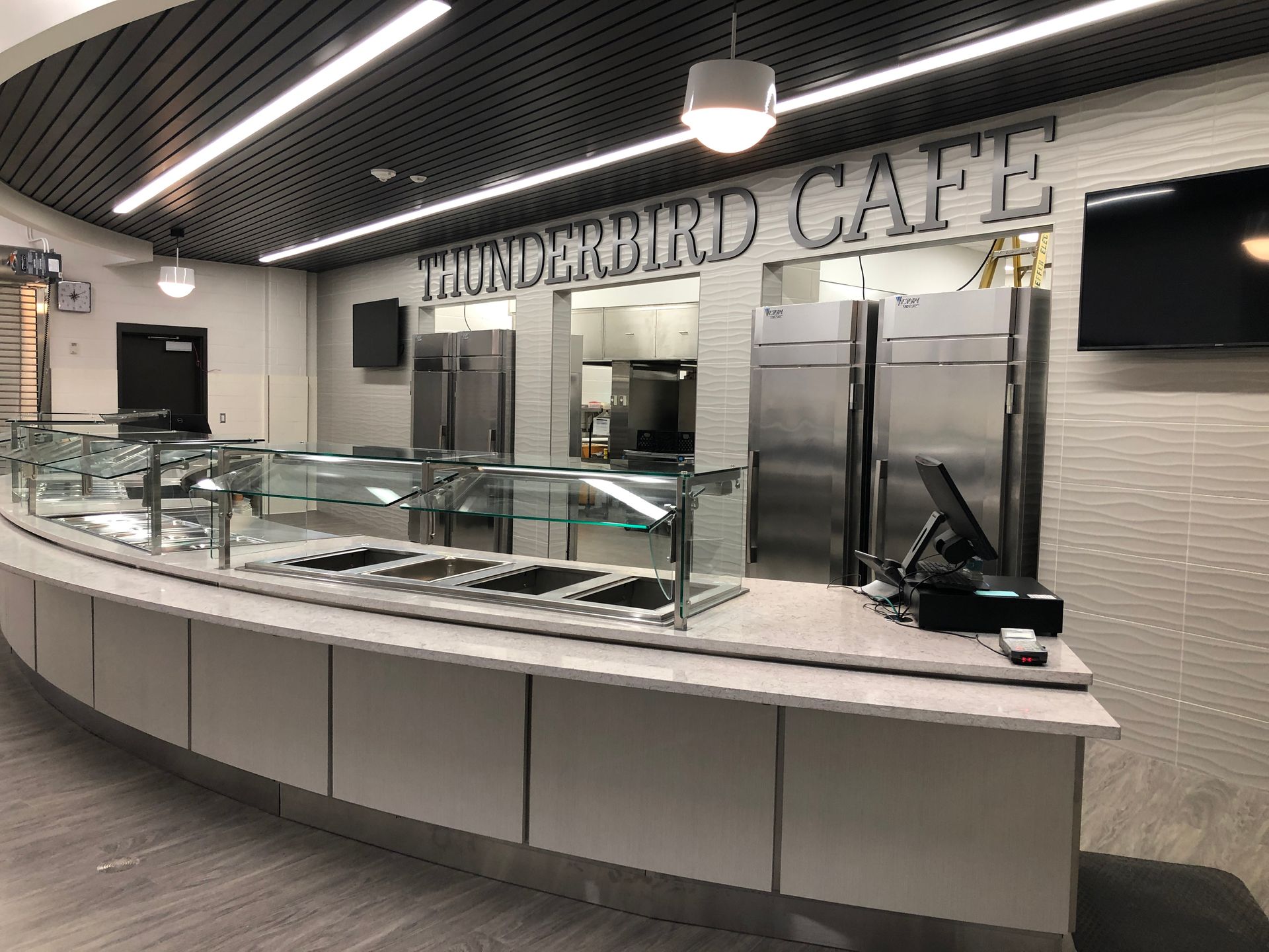 A food service counter inside the Thunderbird Cafe featuring stainless steel appliances and a glass sneeze guard.