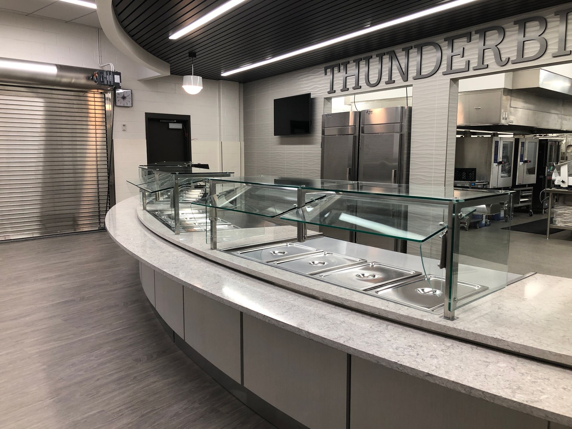 A curved serving counter with glass food guards inside a dining facility with a Thunderbirds sign on the back wall.