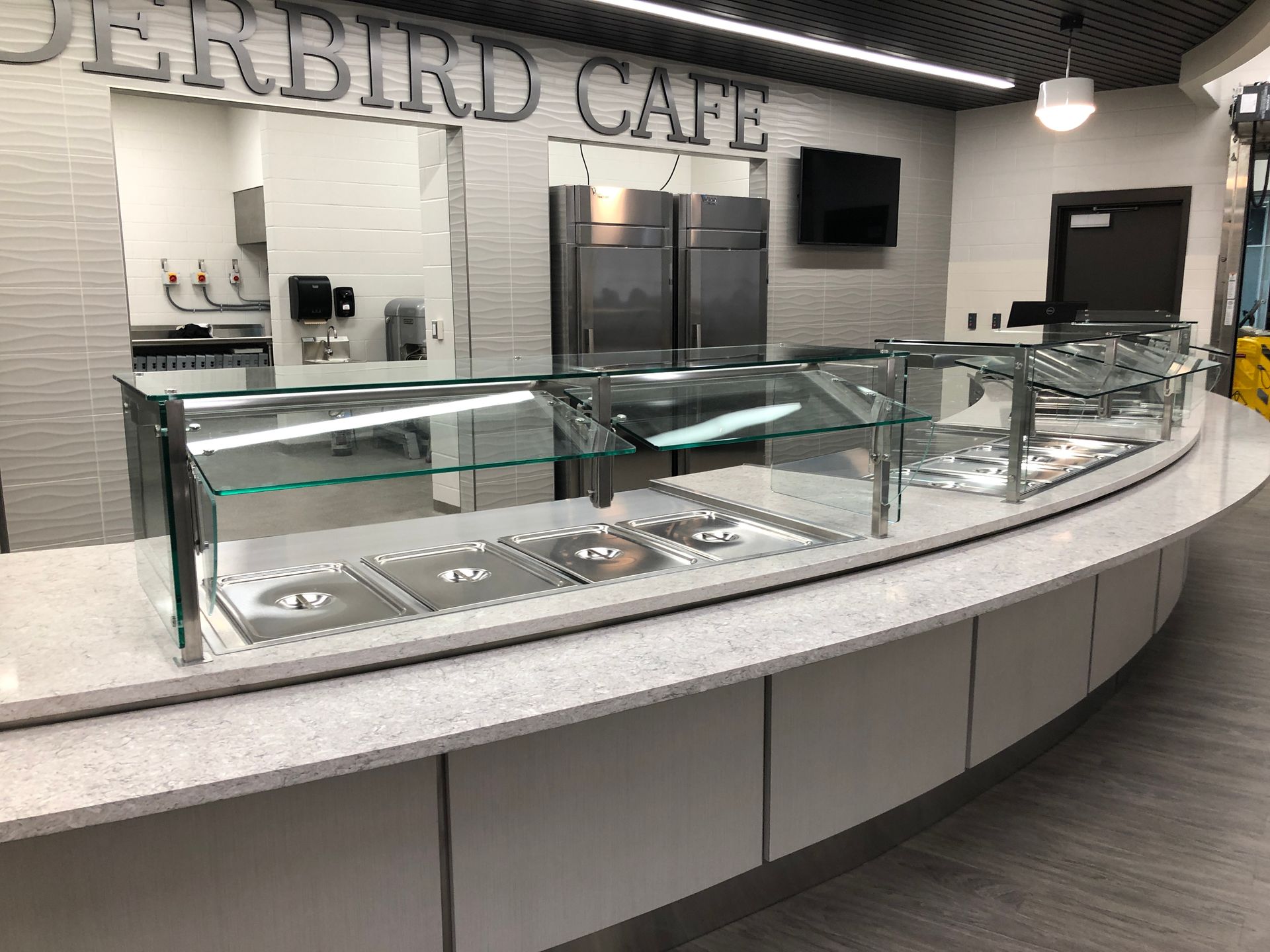 A curved, modern cafeteria service counter with a stone countertop and glass sneeze guards at Thunderbird Cafe.