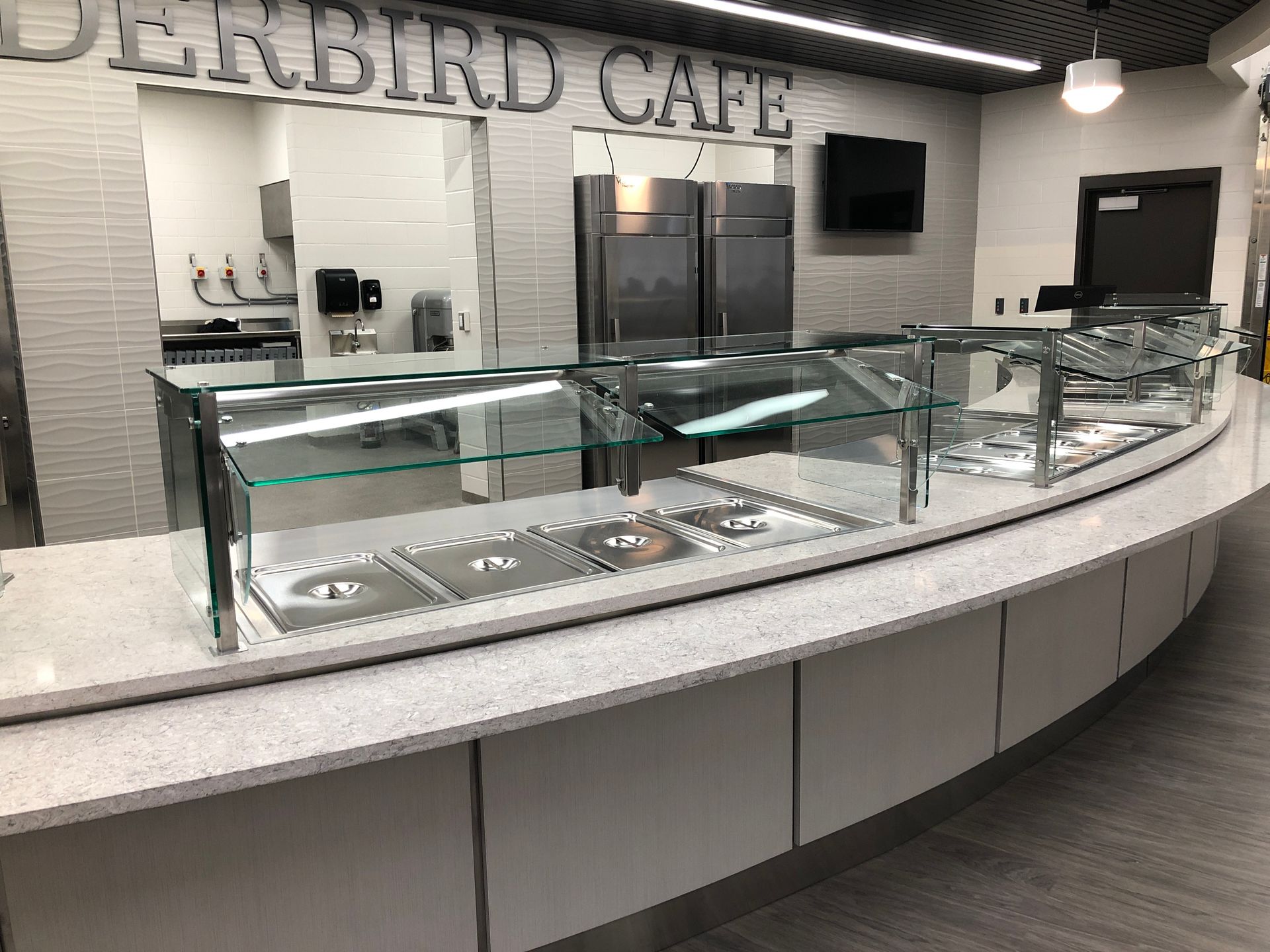 A modern Thunderbird Cafe serving counter with a white speckled countertop, metal food bins, and glass sneeze guards.