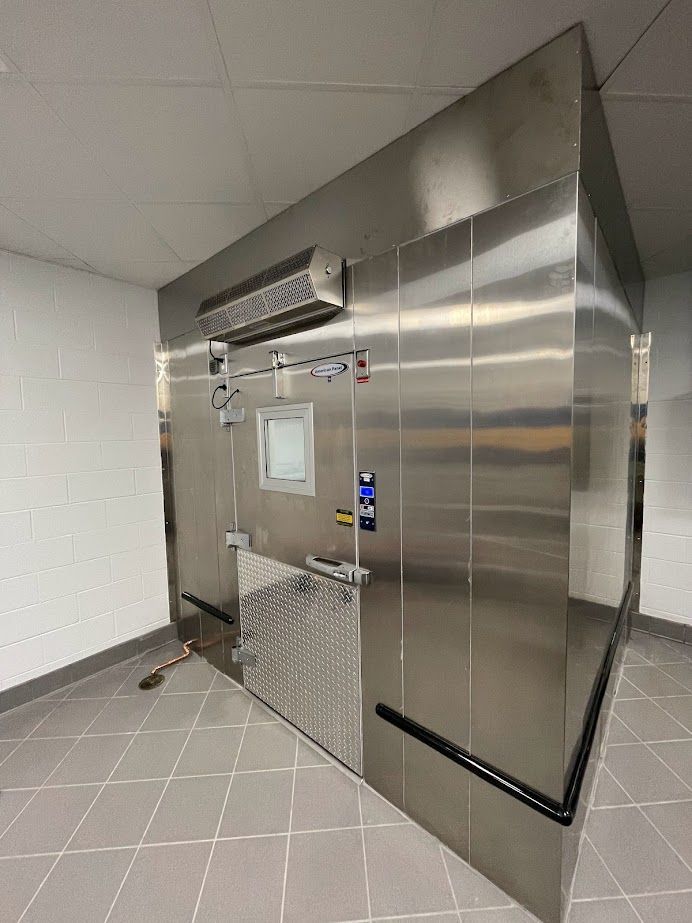 A stainless steel walk-in freezer unit with a windowed door, installed in a room with tiled floors and white walls.