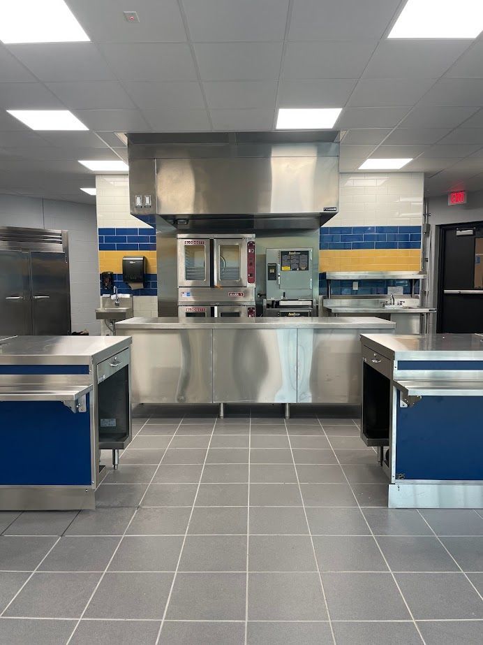 A modern commercial kitchen featuring stainless steel equipment, tiled floors, and blue and yellow wall accents.