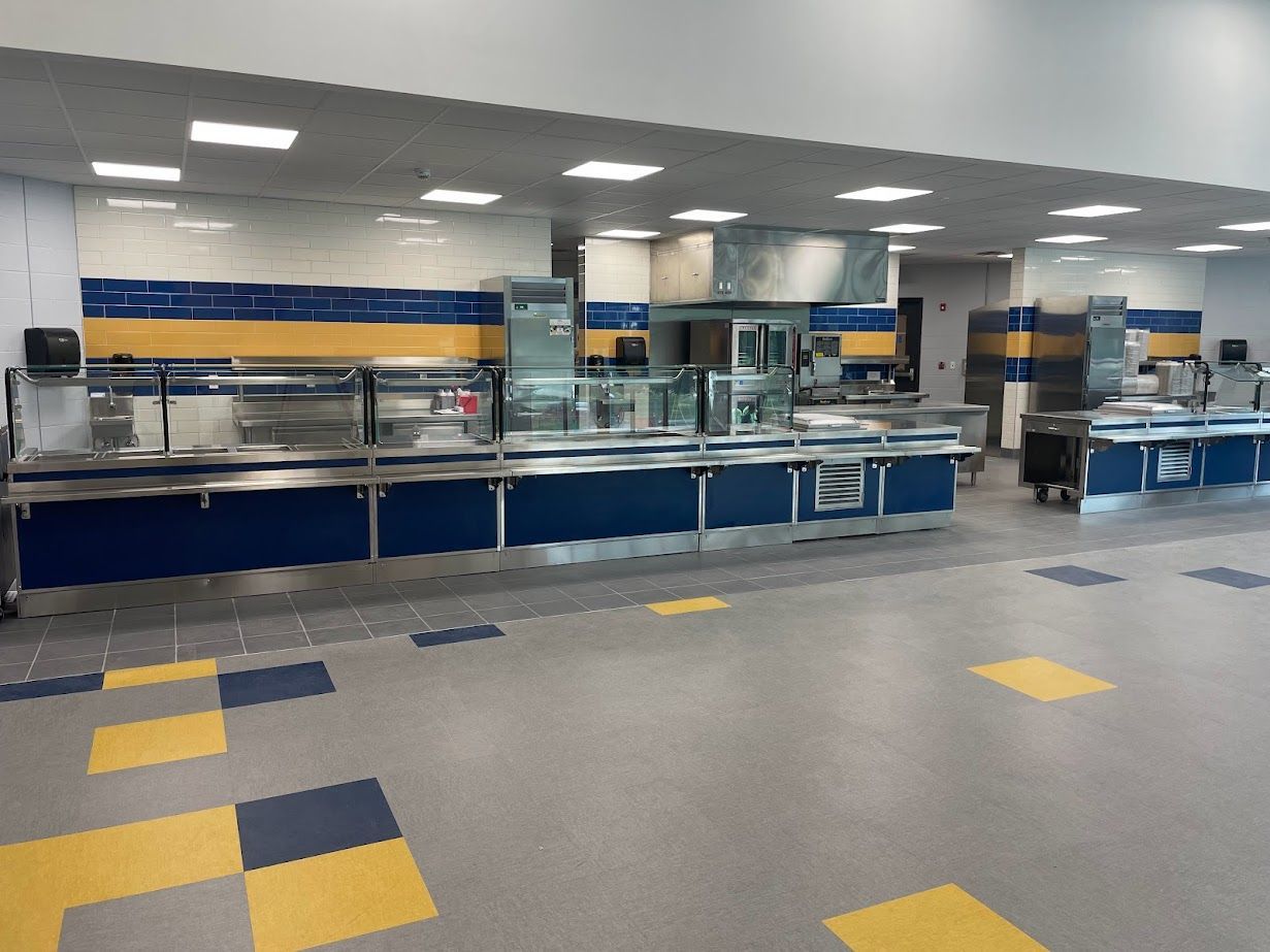 A view of an empty school cafeteria serving line with blue and yellow tile accents and a gray floor.